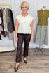 Front view of woman wearing Swagger Boutique’s Cream Sleeveless Button Up Sweater with Kelsey Coated Ankle Flare Jeans in Chocolate by Kut from the Kloth with clothing hanging in the background.
