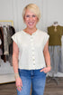 Front view of woman wearing Swagger Boutique’s Cream Sleeveless Button Up Sweater with Maya Denim Jeans by Kut from the Kloth with clothing hanging in the background.