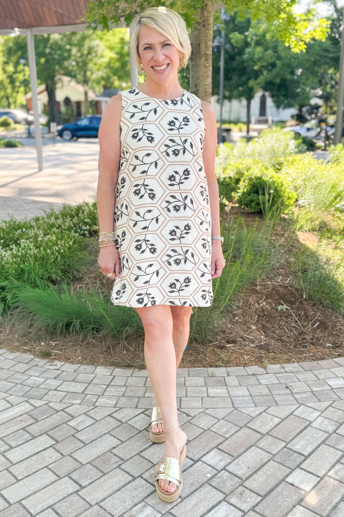 Front view of woman wearing Swagger Boutique’s Cream, Taupe &amp; Black Floral Printed Shift Dress with sandals outside at a park.
