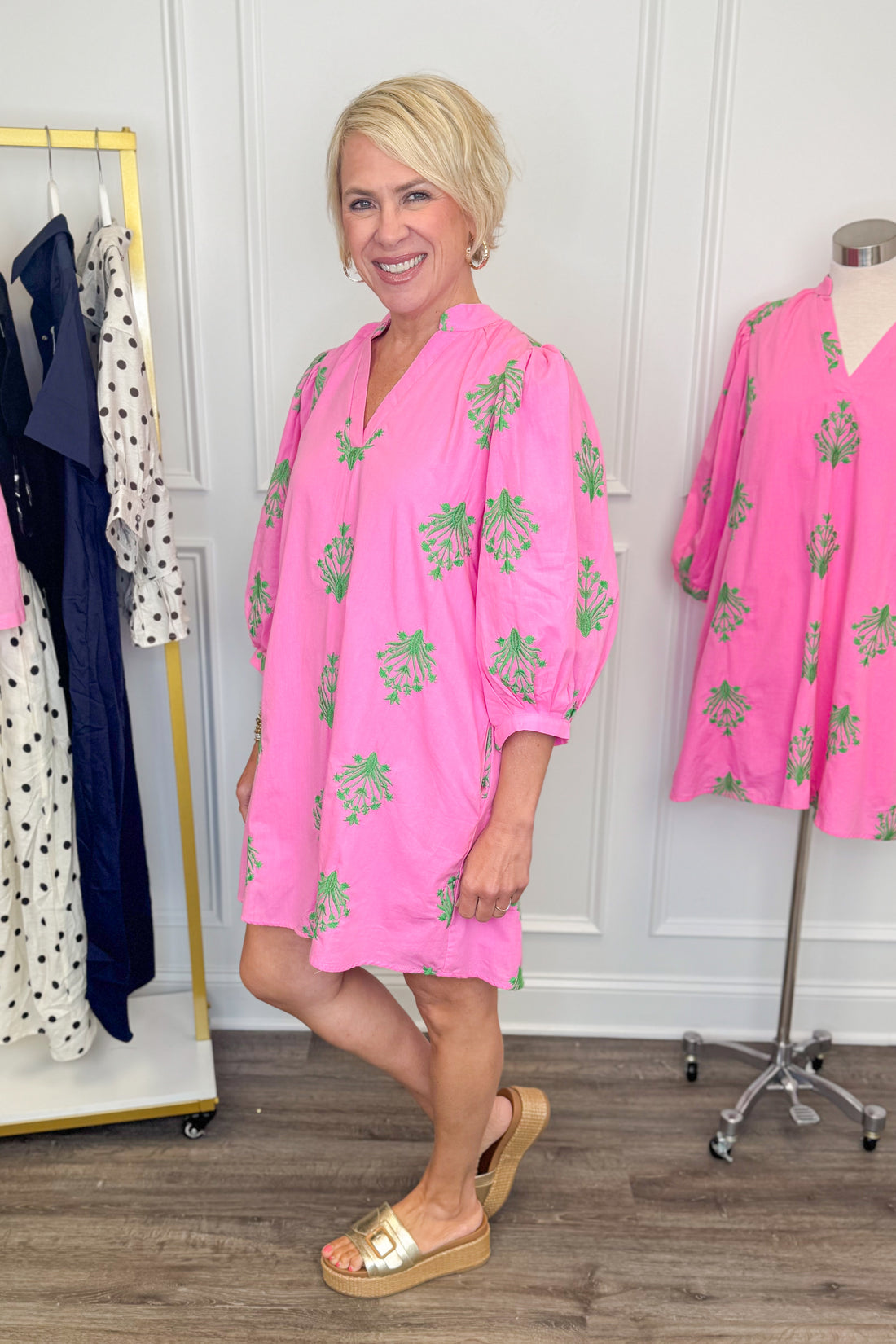 Side view of woman wearing Swagger Boutique’s Pink &amp; Green 3/4 Sleeve Embroidered Dress with sandals with clothes around her.