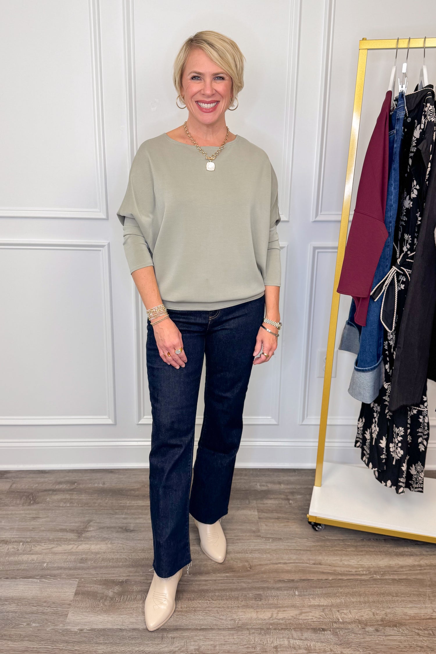 Woman in a green top and blue jeans standing in front of a clothing rack.