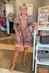 Woman in a patterned dress and brown boots standing in a store setting.