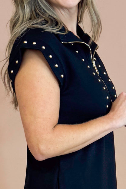 Black sleeveless top with gold embellishments on a beige background