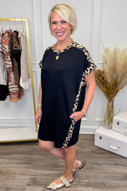 Side view of black short sleeve mini dress showing leopard print contrast trim and side pockets.