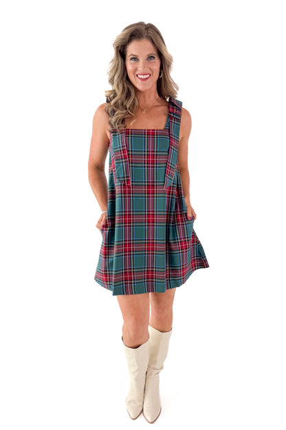 Front view of woman wearing Green Tartan Bow Strap Dress with boots against white studio background.