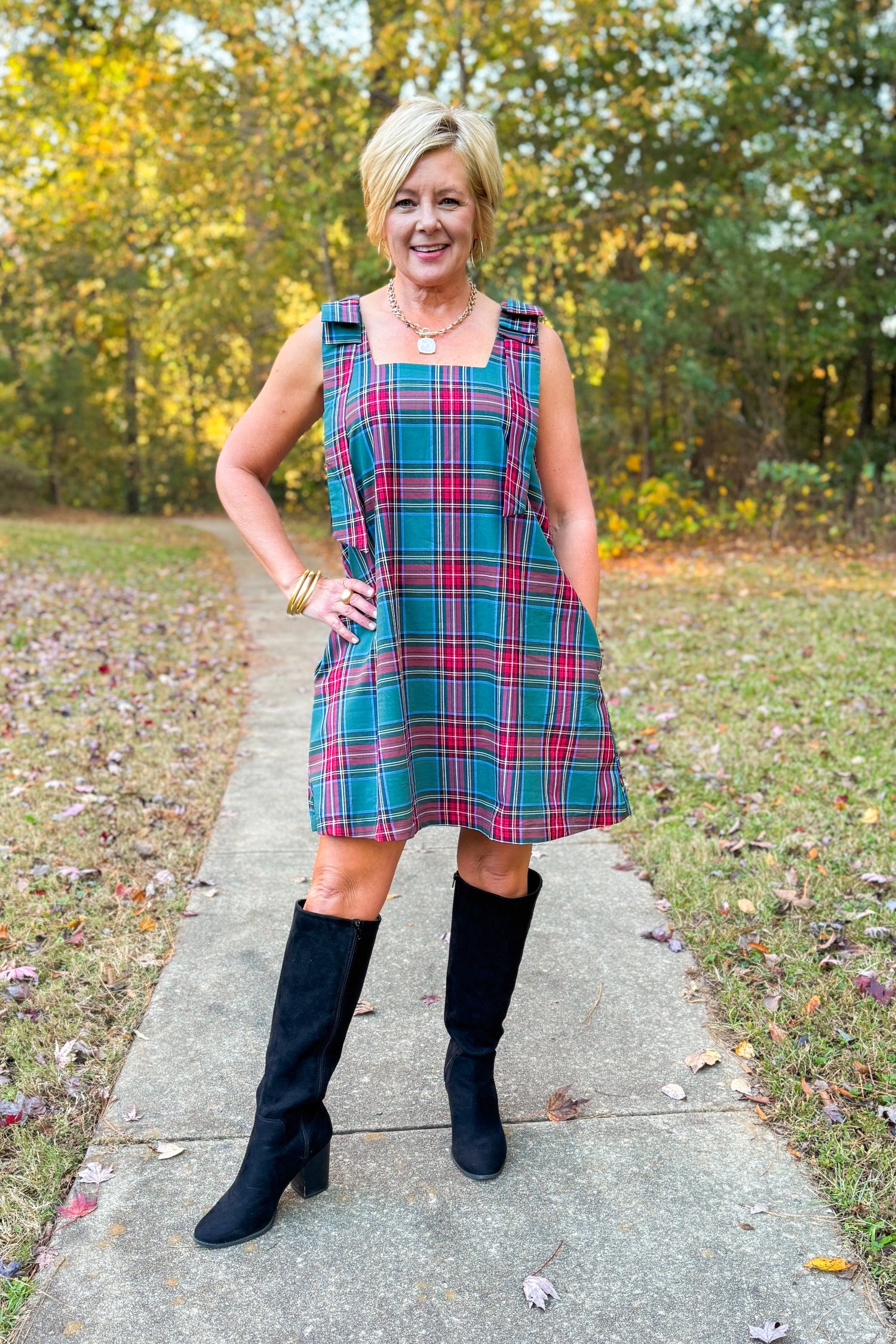 Front view of woman wearing Green Tartan Bow Strap Dress with boots outside.