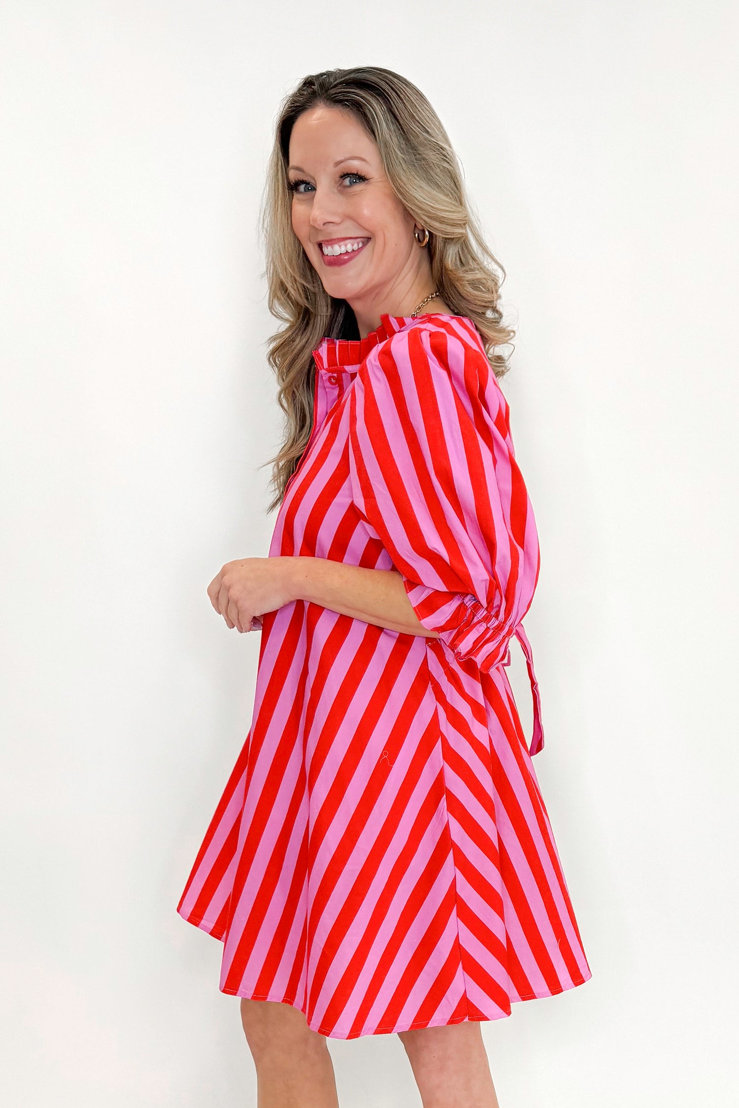Side view of woman wearing Pink &amp; Red Striped Tie Back Dress by Entro with sandals against white studio background.