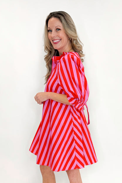 Side view of woman wearing Pink &amp; Red Striped Tie Back Dress by Entro with sandals against white studio background.