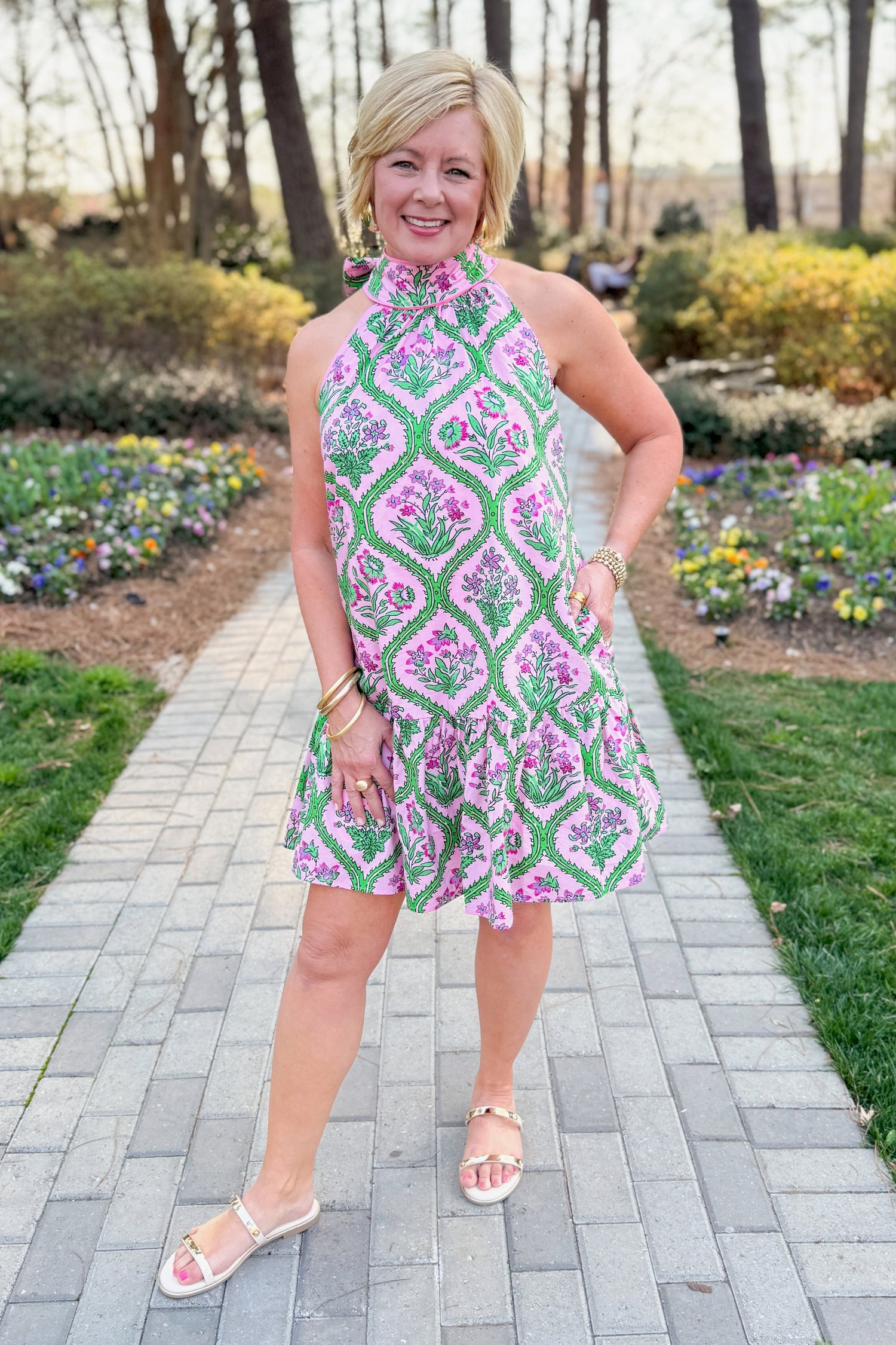 Front view of woman wearing Pink &amp; Green Floral Halter Neck Dress by Entro with sandals at a garden.