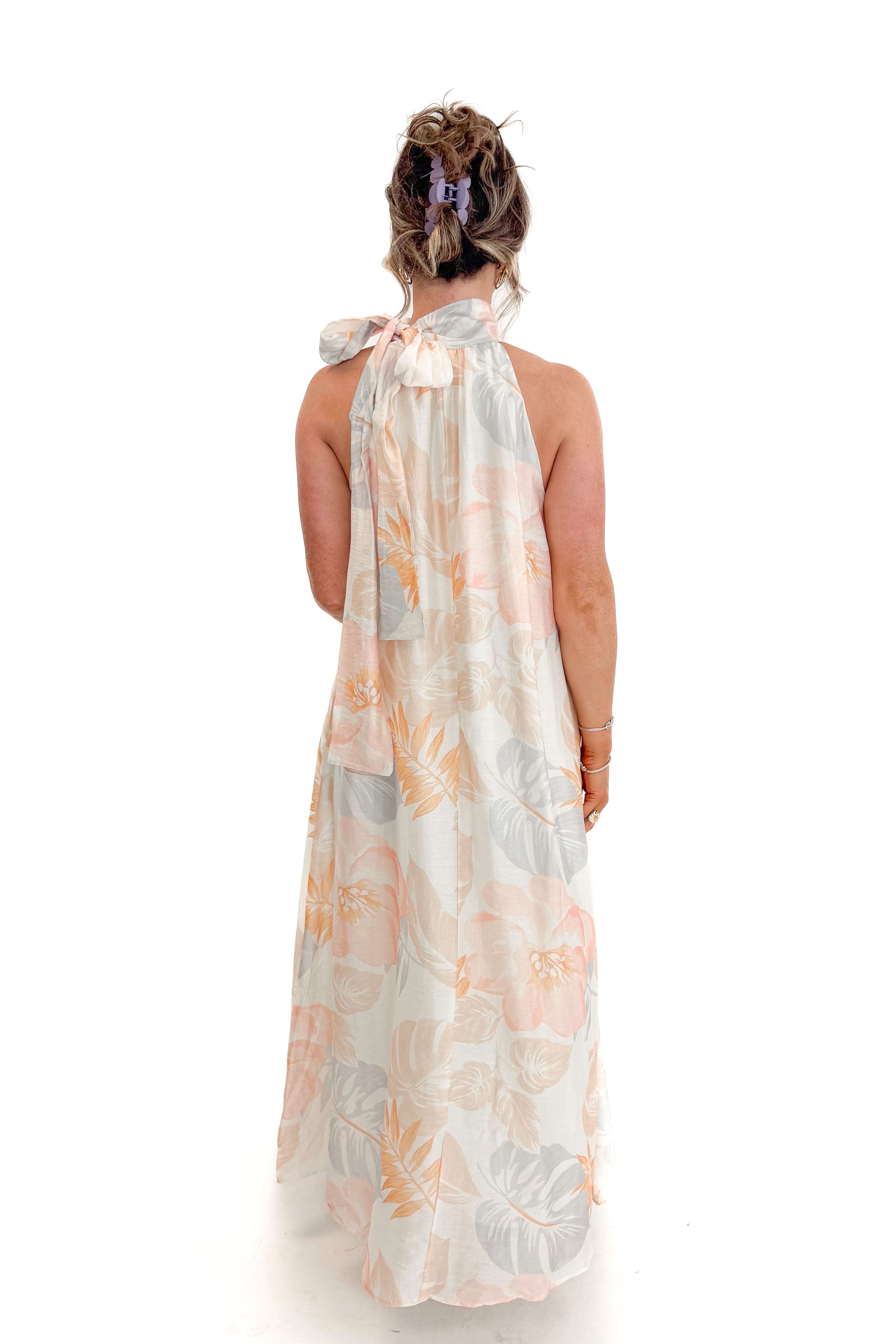 Back view of woman wearing Multi Tropical Printed Tie Neck Maxi Dress by Entro with sandals against white studio background.