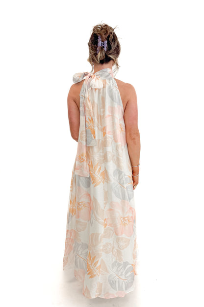 Back view of woman wearing Multi Tropical Printed Tie Neck Maxi Dress by Entro with sandals against white studio background.