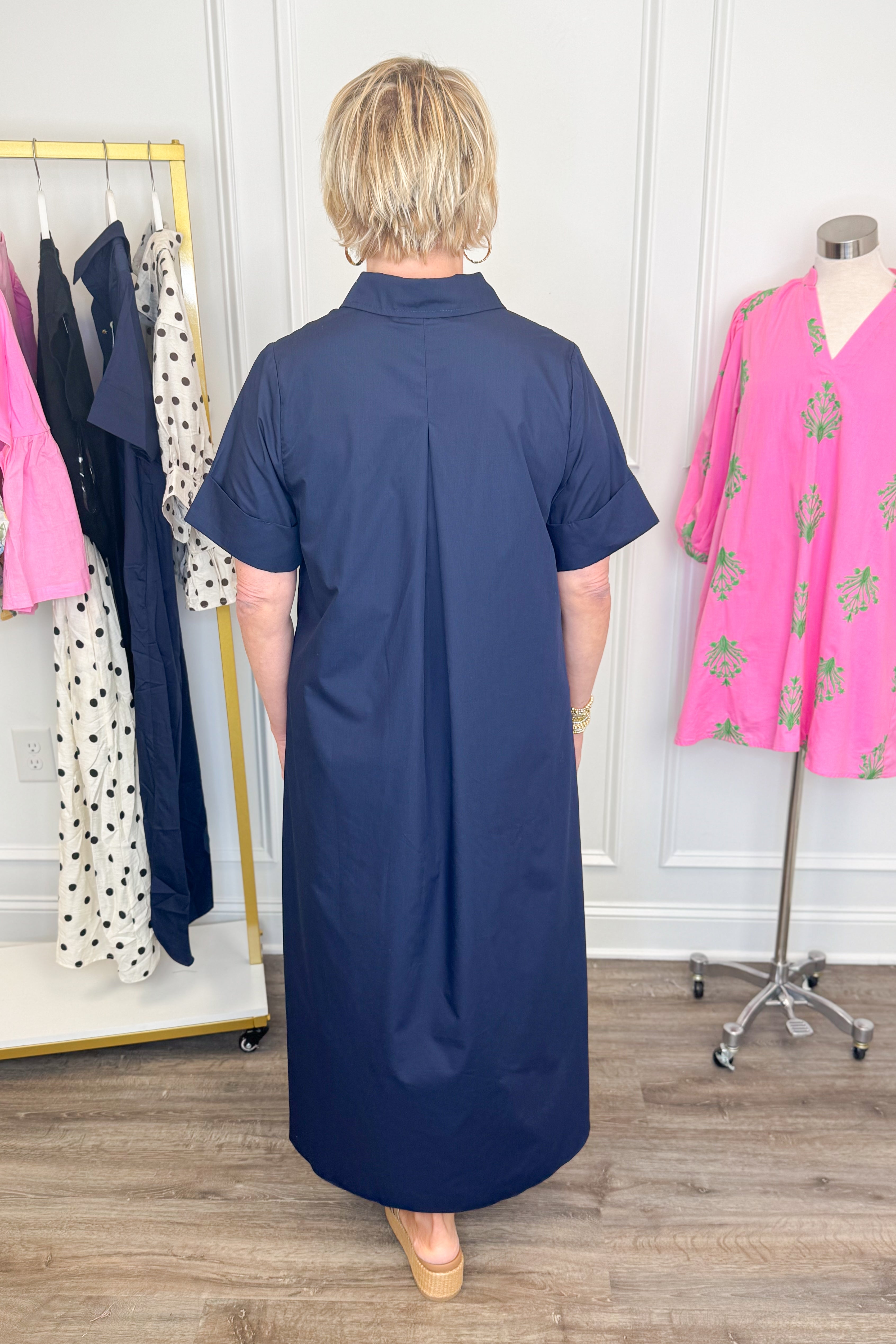 Back view of woman wearing Swagger Boutique’s Navy Collared Midi Dress by Entro with platform sandals with clothes near her. 