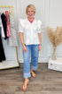 Woman wearing a white blouse and blue jeans in a room with a clothing rack and decorative items.