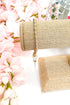 Gold beaded bracelet on a white surface with pink flowers in the background