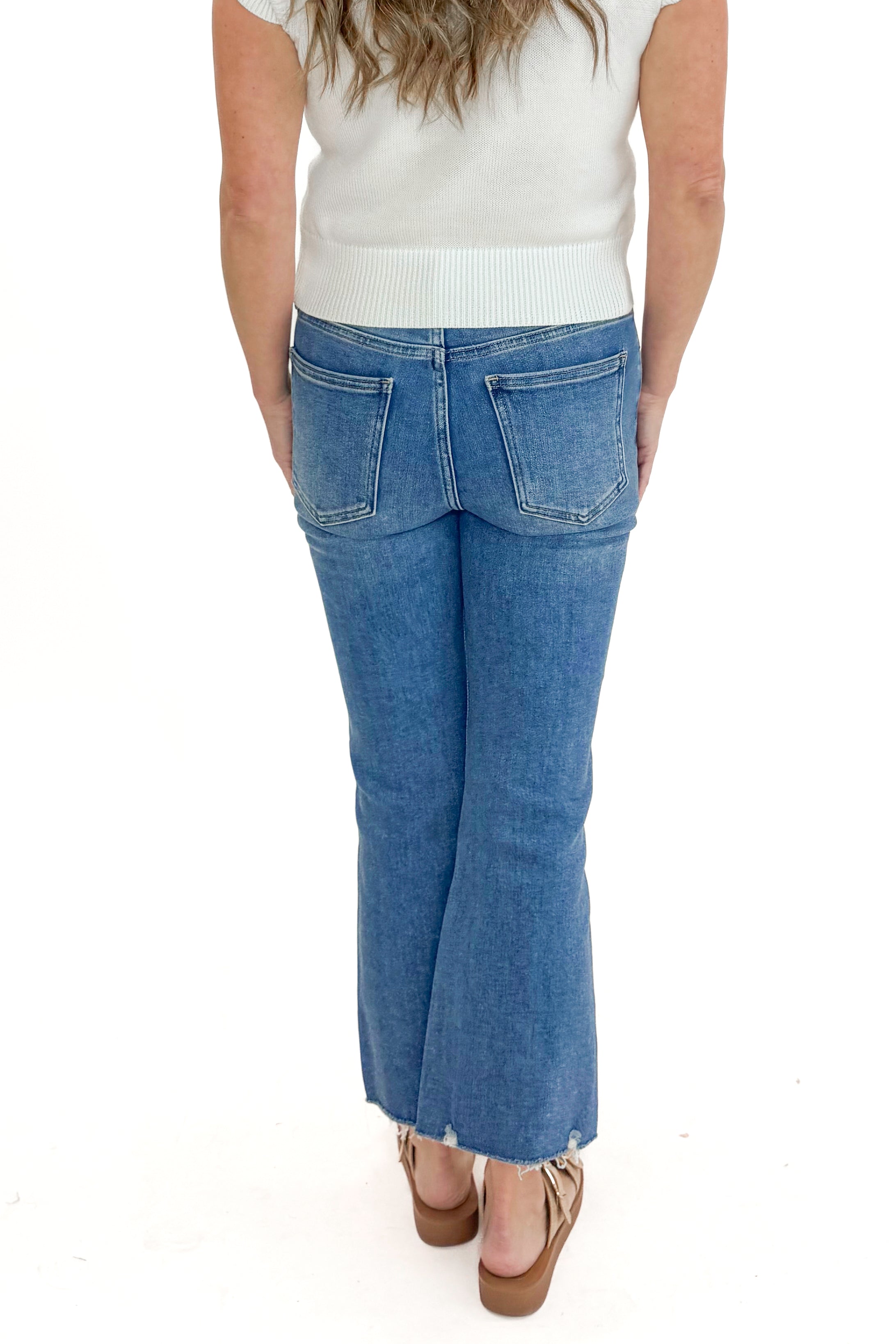 Back view of woman wearing Medium Wash Kick Crop Jeans by Just Black Denim with sweater against white studio background.