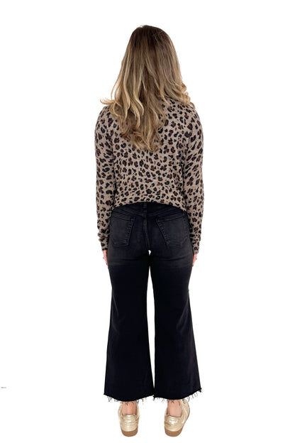 Back view of woman wearing washed black jeans and print top against white studio background.