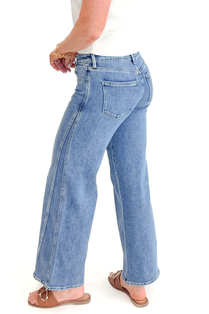 Side view of woman wearing Medium Wash Seam Detail Wide Leg Jeans by Just Black Denim with white top against white studio background.