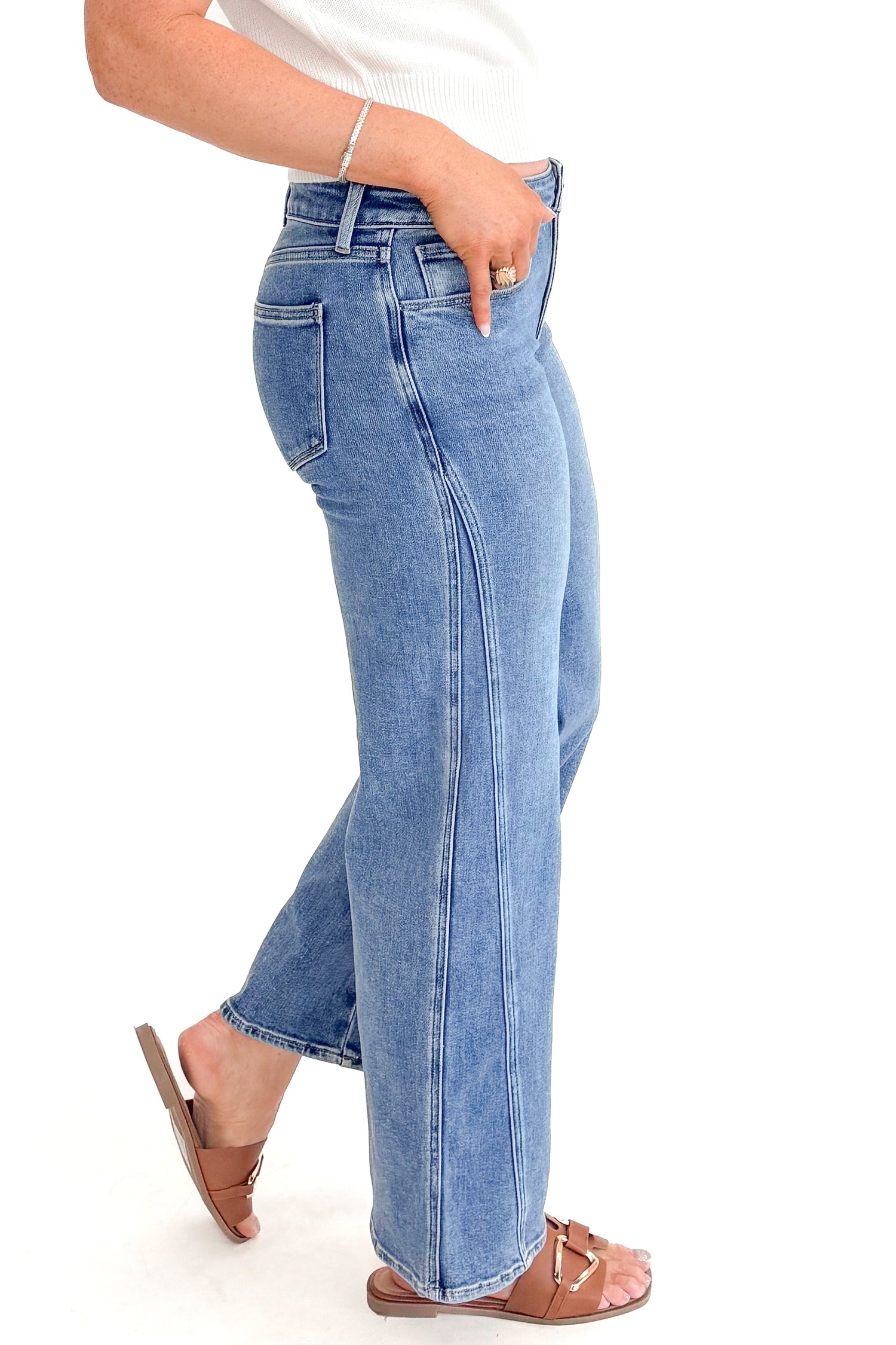 Side view of woman wearing Medium Wash Seam Detail Wide Leg Jeans by Just Black Denim with white top against white studio background.