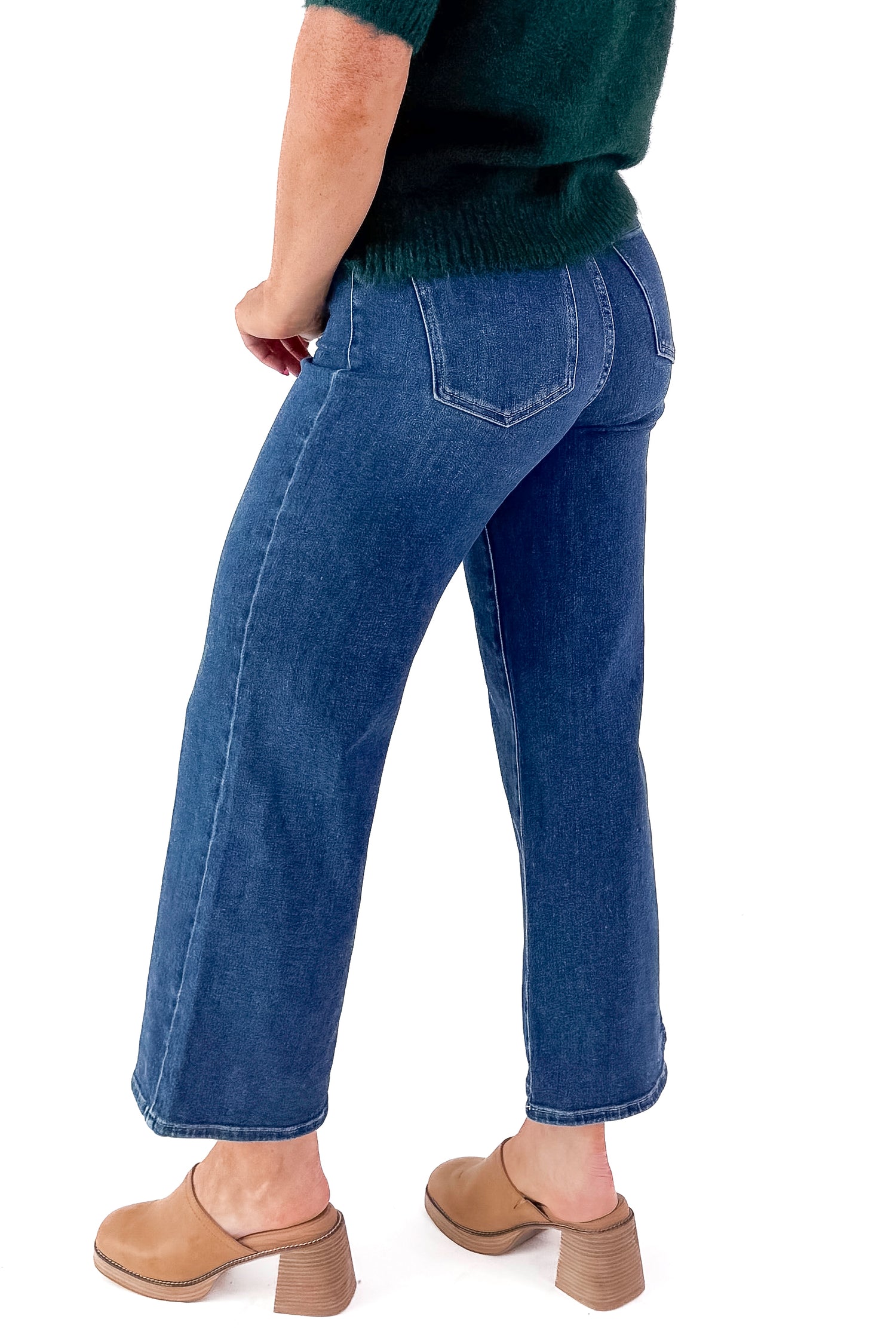 Side view of woman wearing green sweater with Dark Wash No Pocket Trouser Jeans against white studio background.