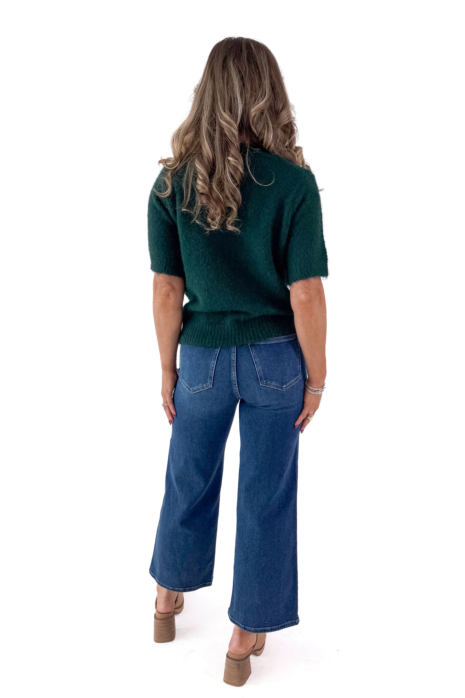 Back view of woman wearing green sweater with Dark Wash No Pocket Trouser Jeans against white studio background.