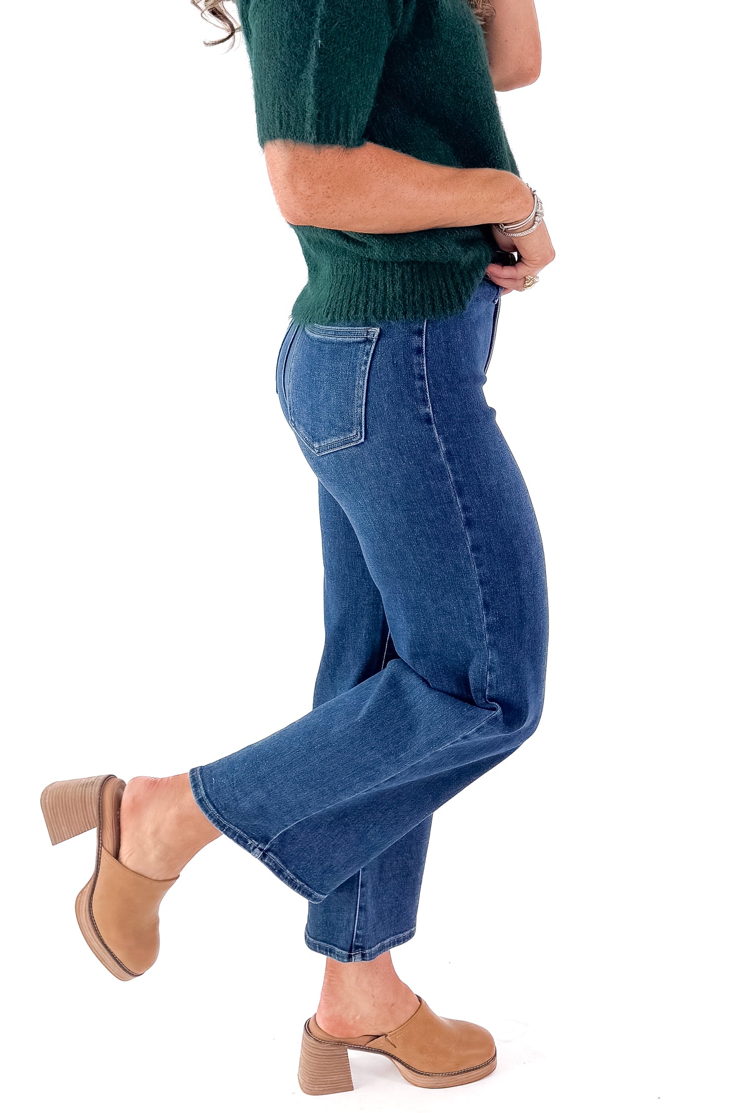 Side view of woman wearing green sweater with Dark Wash No Pocket Trouser Jeans against white studio background.