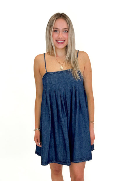 Front view of woman wearing Denim Pleat Detail Tank Dress with sandals against white studio background.