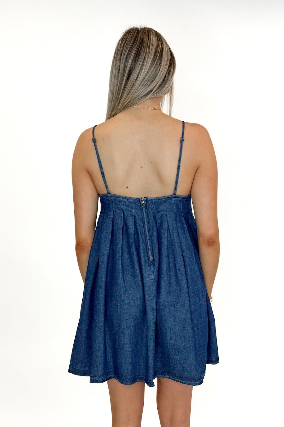 Back view of woman wearing Denim Pleat Detail Tank Dress with sandals against white studio background.