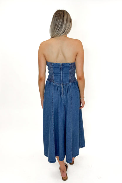 Back view of woman wearing Denim V-Waist Midi Dress with sandals against white studio background.