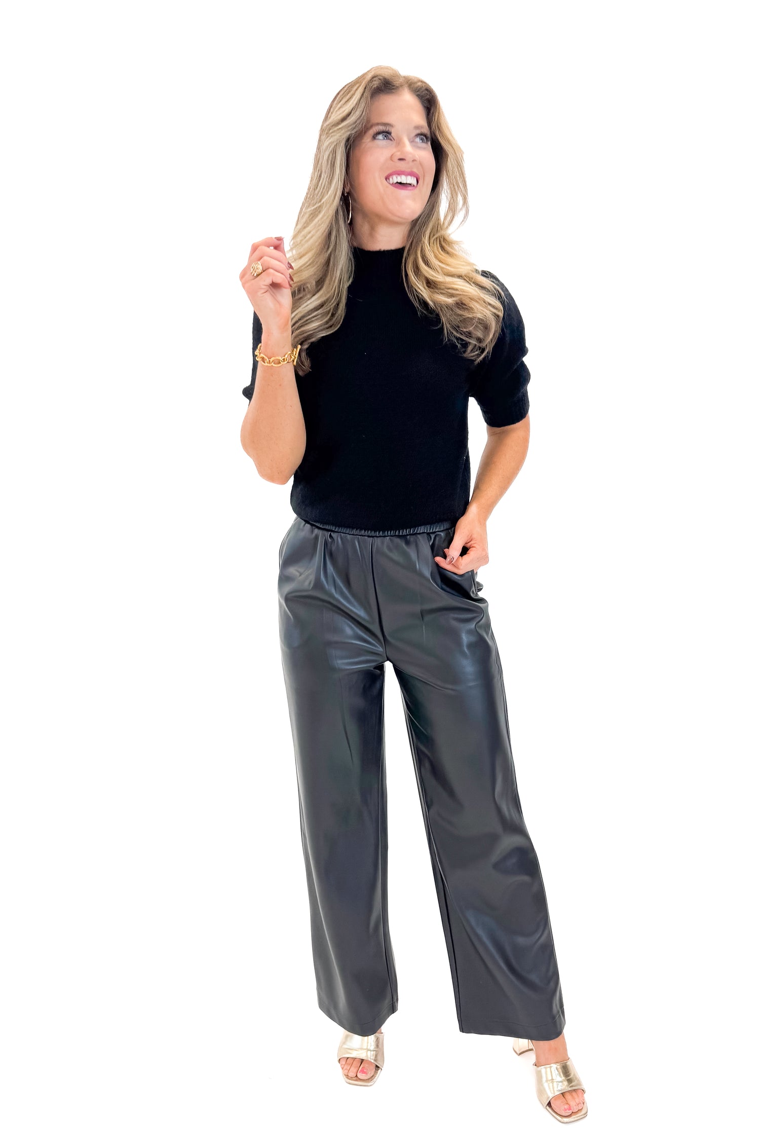 Front view of woman wearing Black Puff Short Sleeve Sweater with Black Faux Leather Pants against white studio background.