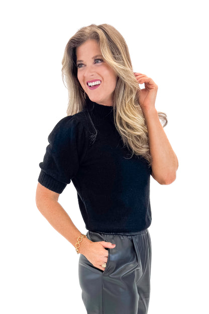Side view of woman wearing Black Puff Short Sleeve Sweater with Black Faux Leather Pants against white studio background.