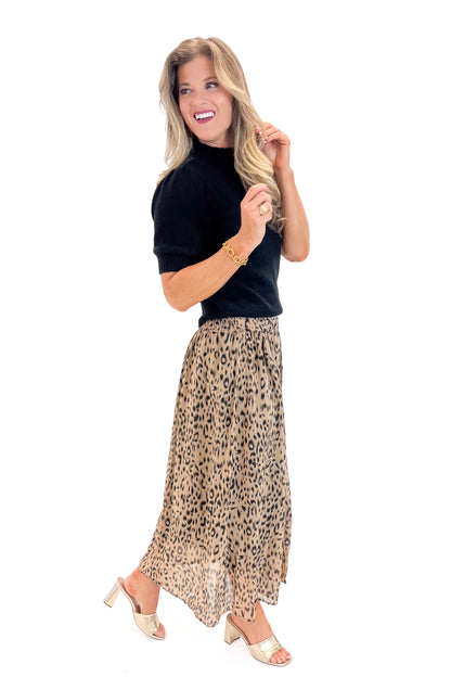 Side view of woman wearing Black Puff Short Sleeve Sweater with Beige Leopard Button Detail Skirt against white studio background.