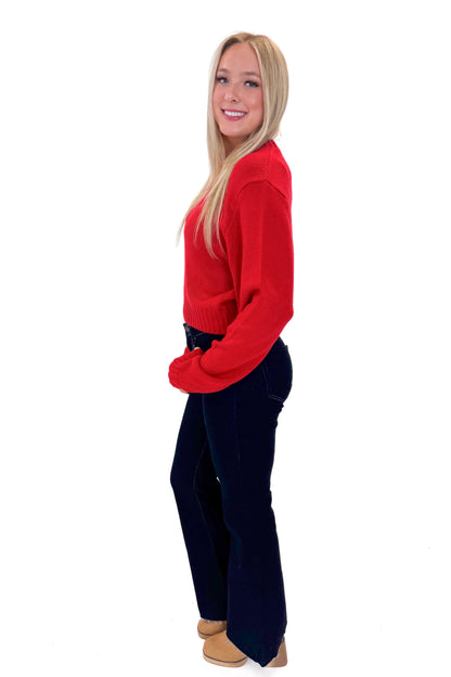 Side view of woman wearing Red Ribbed Neck Sweater with jeans against white studio background.