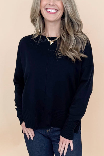 Front detailed view of woman wearing black long sleeve sweater with jeans against tan studio background.