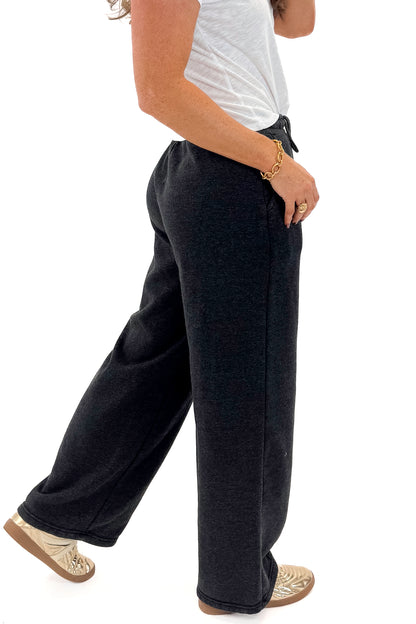 Side view of woman wearing Washed Black Drawstring Sweatpants with white top against white studio background.