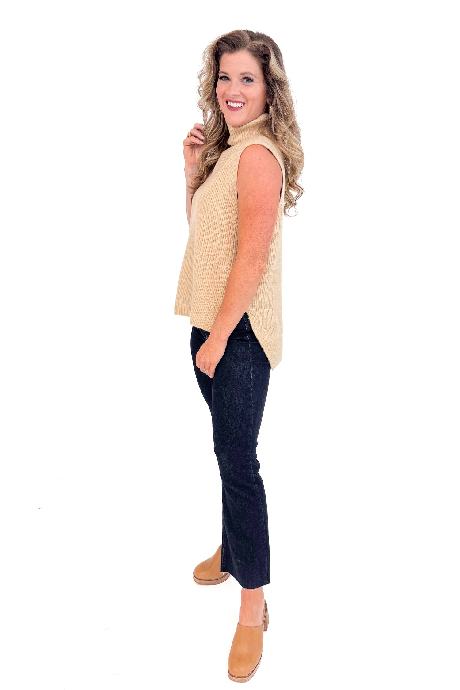 Side view of woman wearing Taupe Turtleneck Sweater Vest and jeans with a white background.