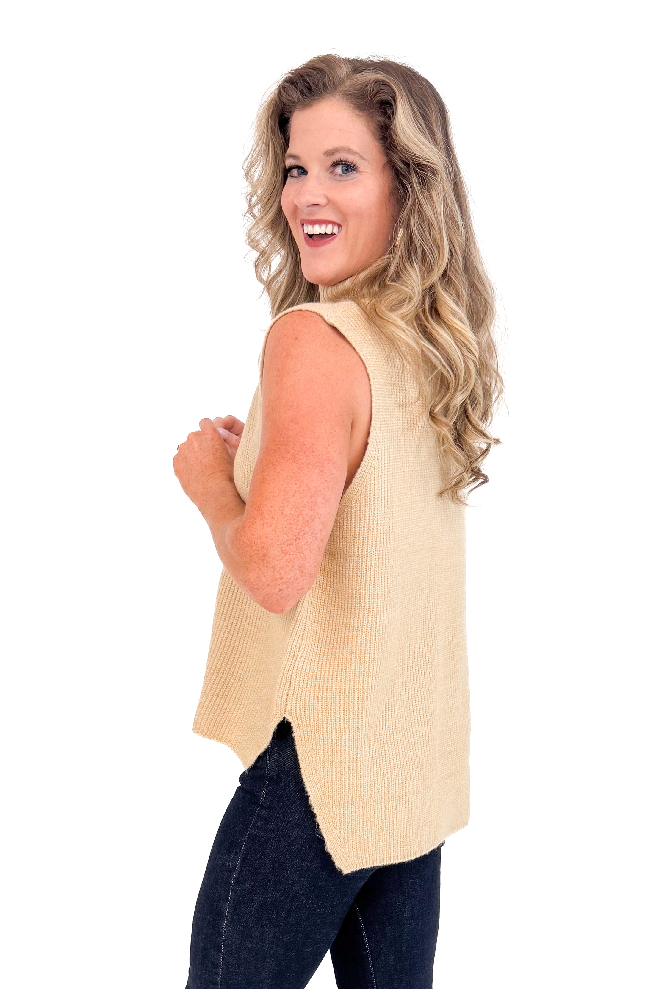 Side studio picture of woman wearing Taupe Turtleneck Sweater Vest and jeans with a white background.