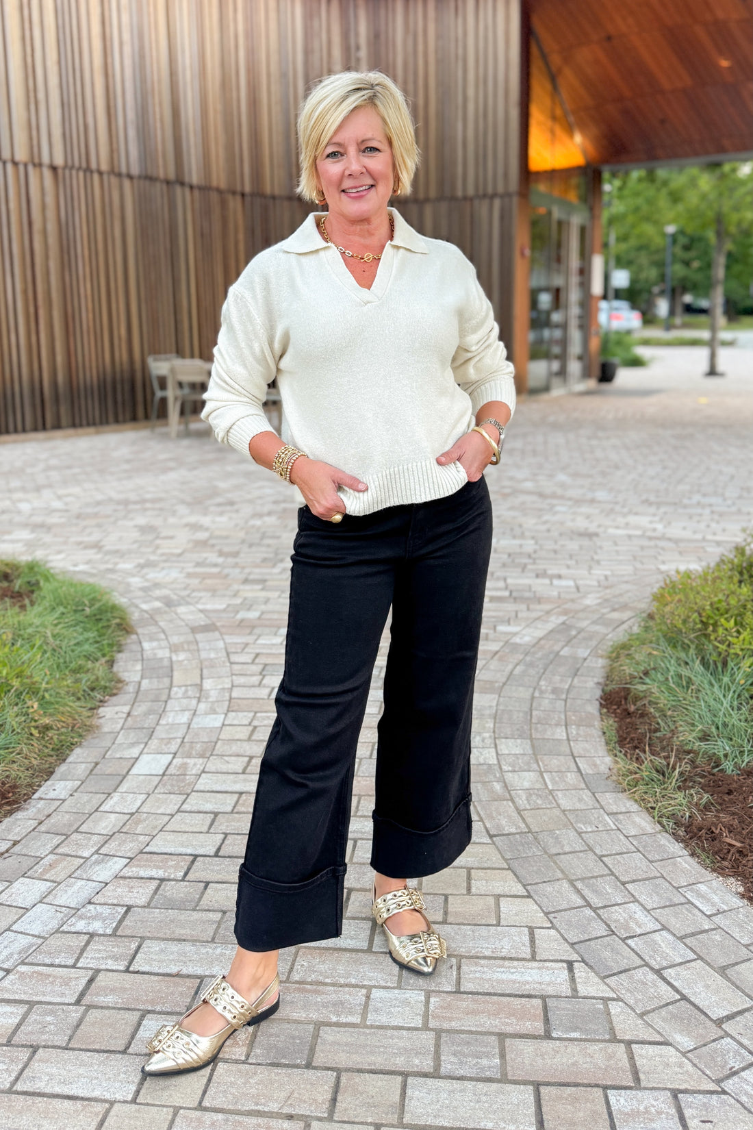 Woman in a white sweater and black pants standing on a paved walkway.