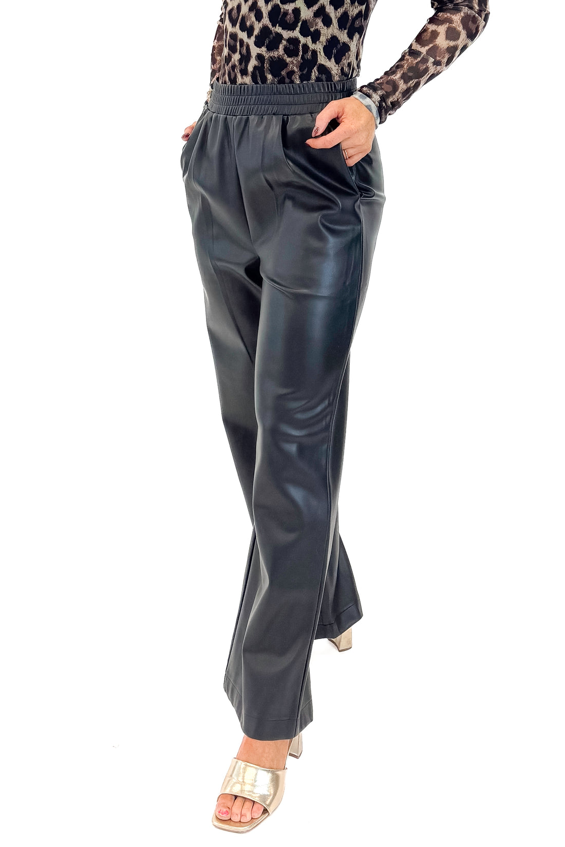 Front detail view of woman wearing Black Faux Leather Pants with leopard mesh top against white studio background.