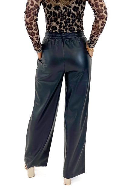 Back view of woman wearing Black Faux Leather Pants with leopard mesh top against white studio background.