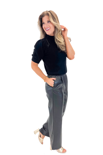 Side view of woman wearing Black Faux Leather Pants with black sweater against white studio background.