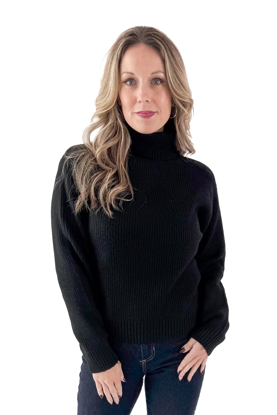 Front view of woman wearing black sweater with jeans against white studio background.