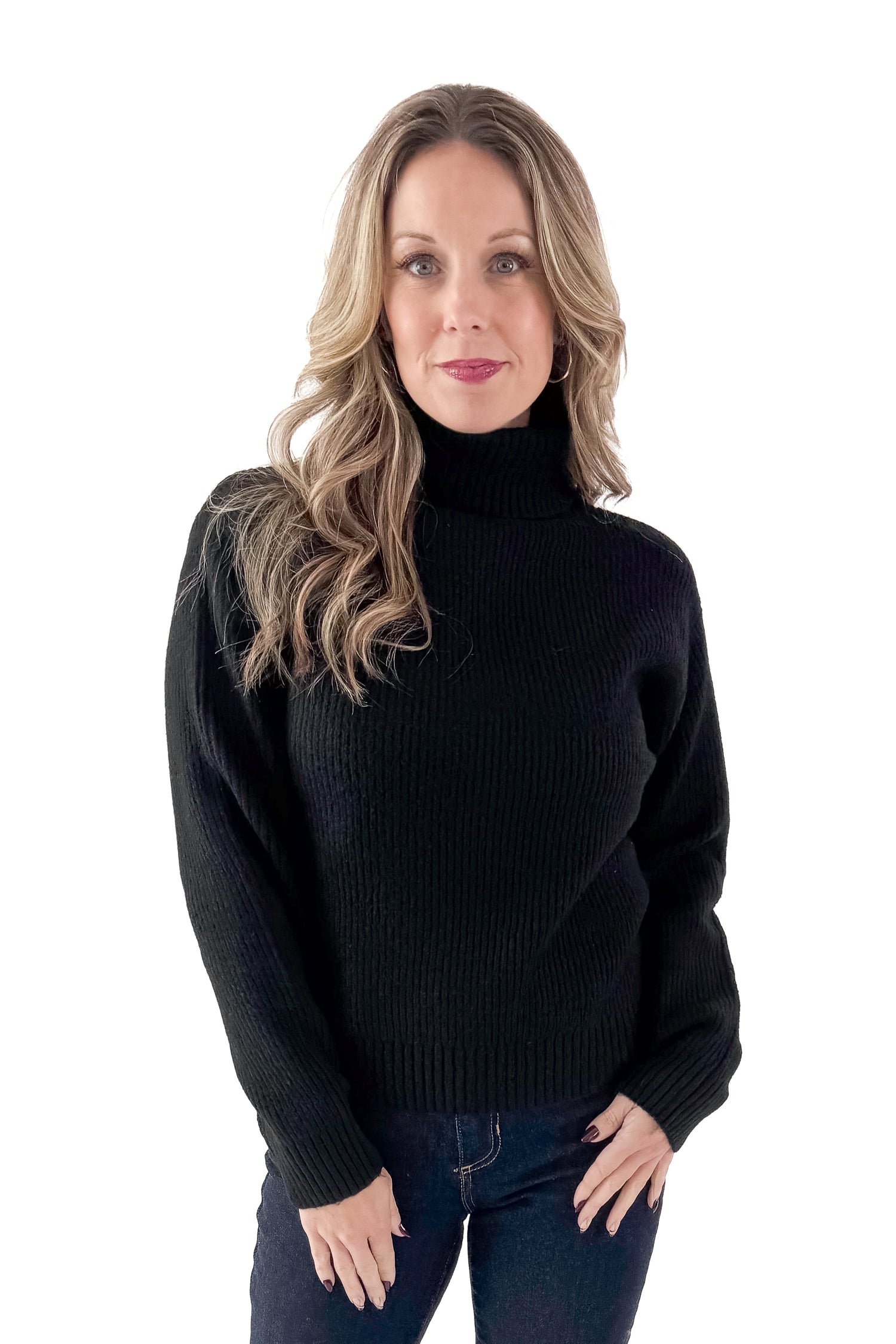 Front view of woman wearing black sweater with jeans against white studio background.