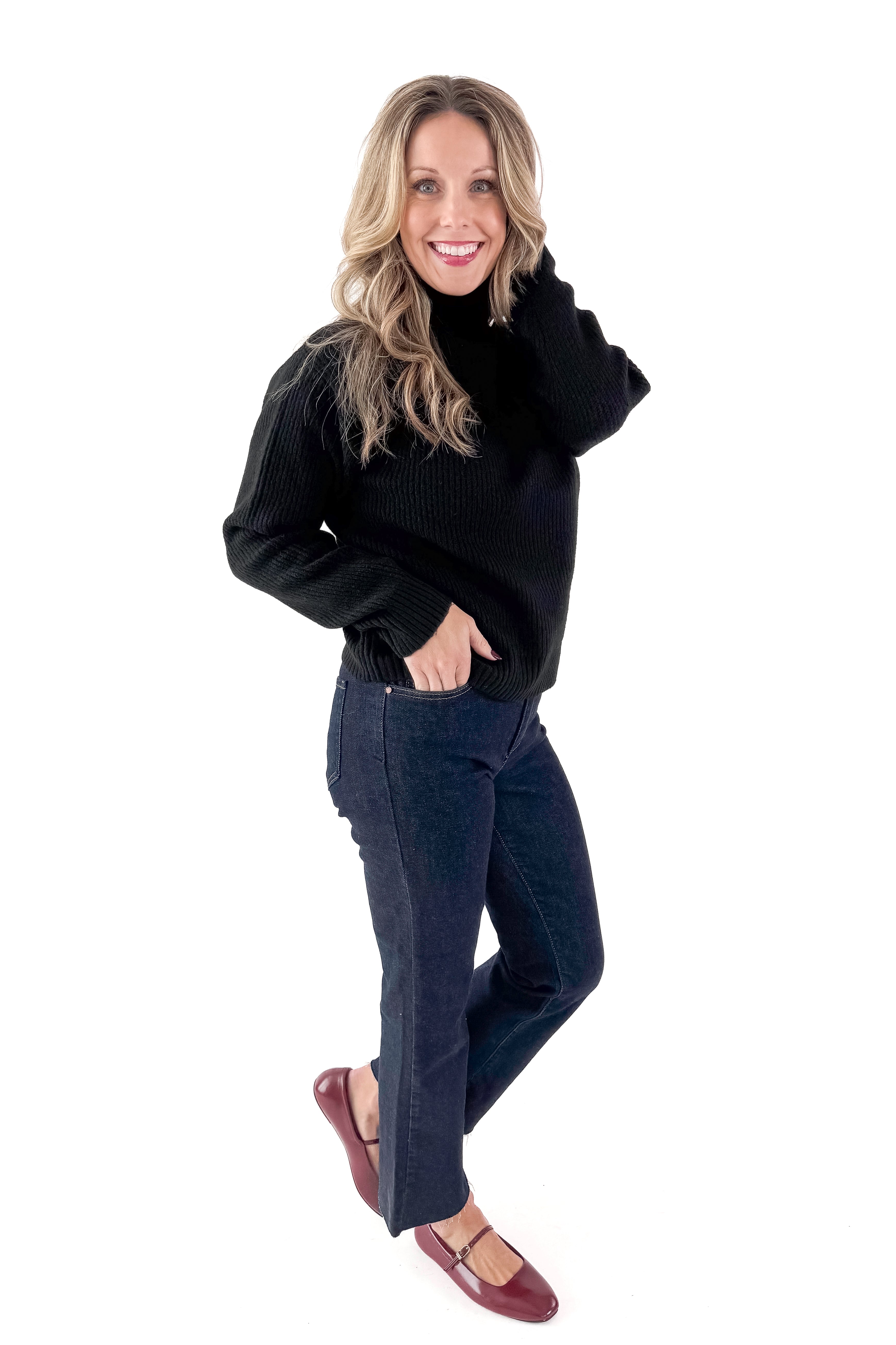 Front view of woman wearing black sweater with jeans against white studio background.