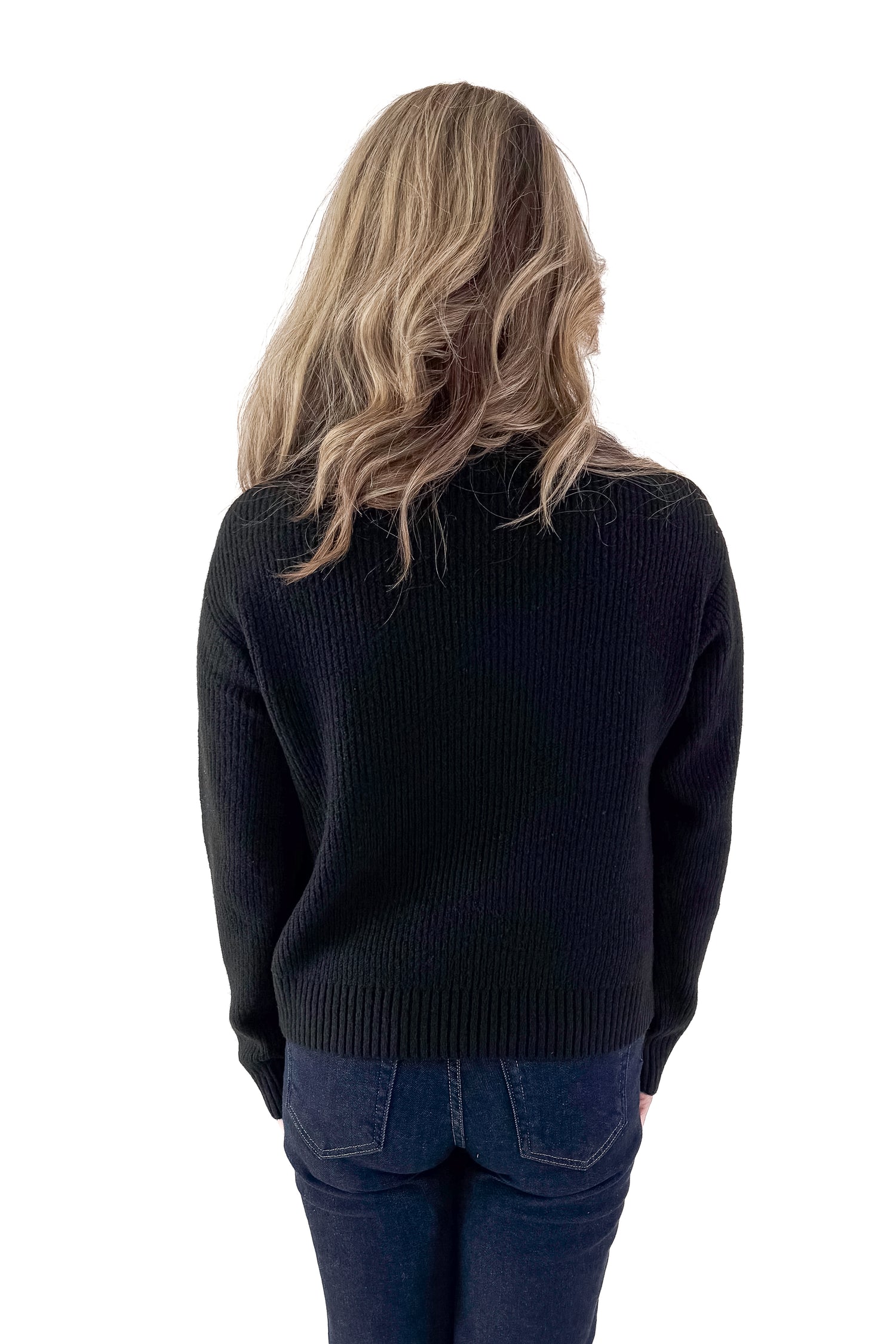 Front view of woman wearing black sweater with jeans against white studio background.