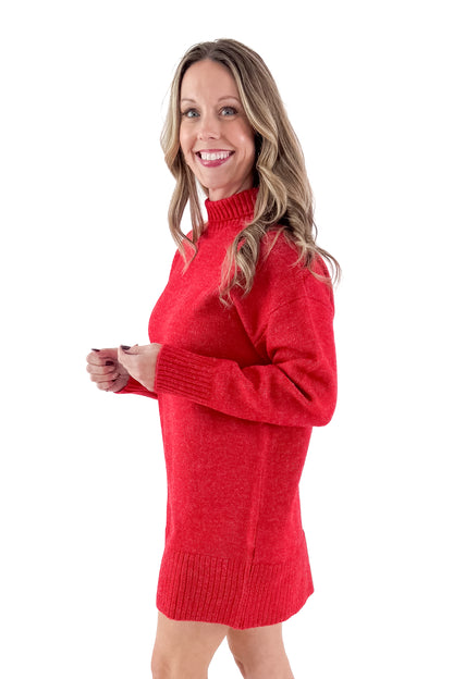 Side view of woman wearing red sweater dress with boots against white studio background.