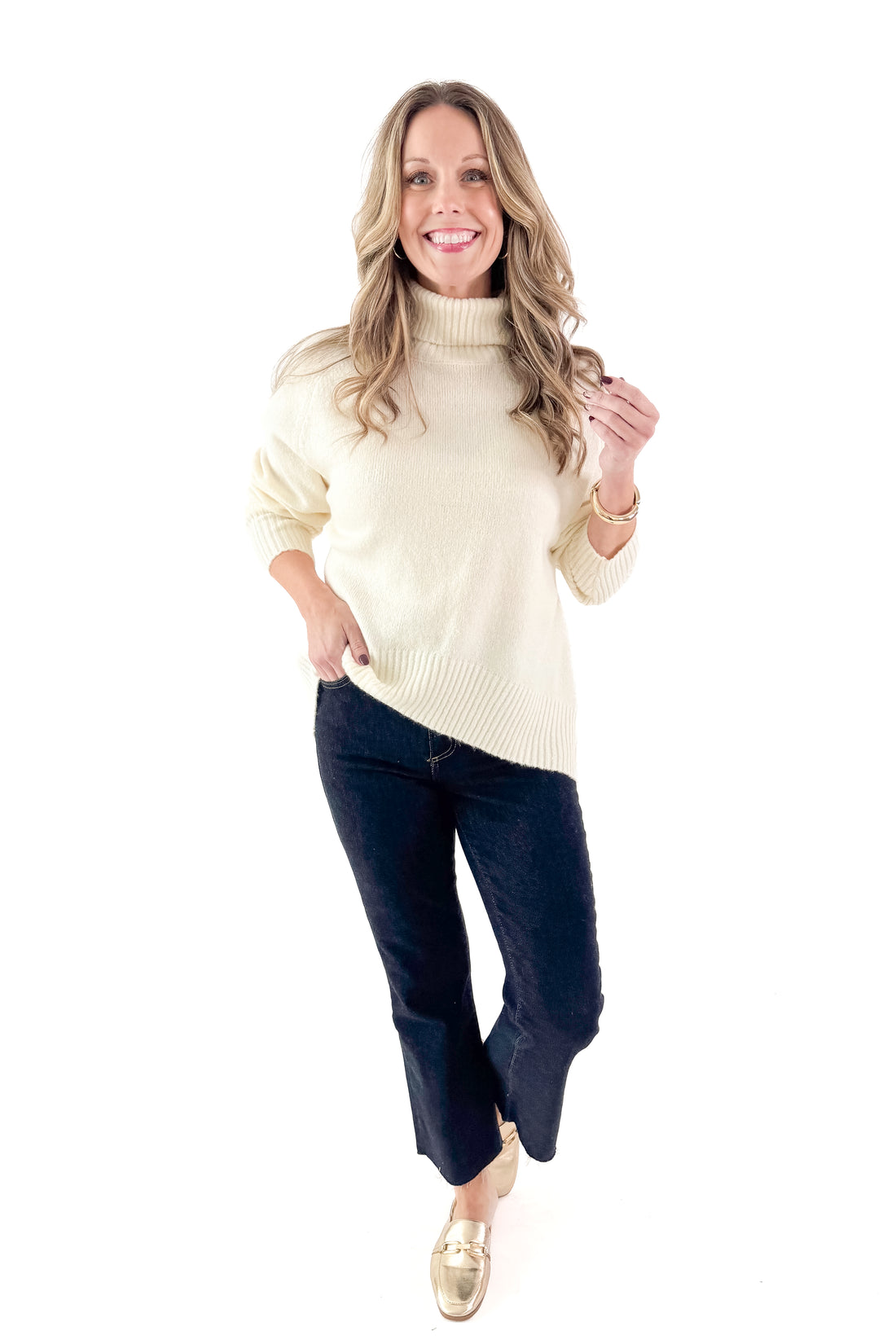 Front view of woman wearing Cream Turtleneck Sweater with jeans against white studio background.
