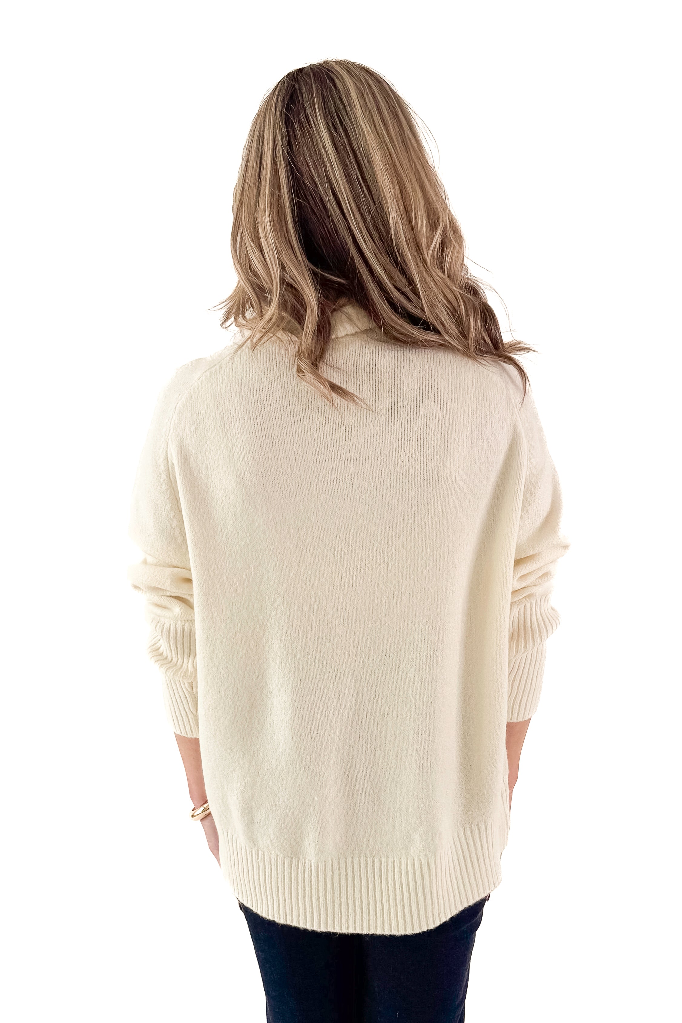 Back view of woman wearing Cream Turtleneck Sweater with jeans against white studio background.