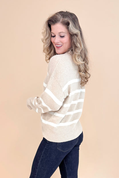 Side view of studio picture of woman wearing Taupe and Cream Striped Mock Neck Sweater and jeans with tan background.