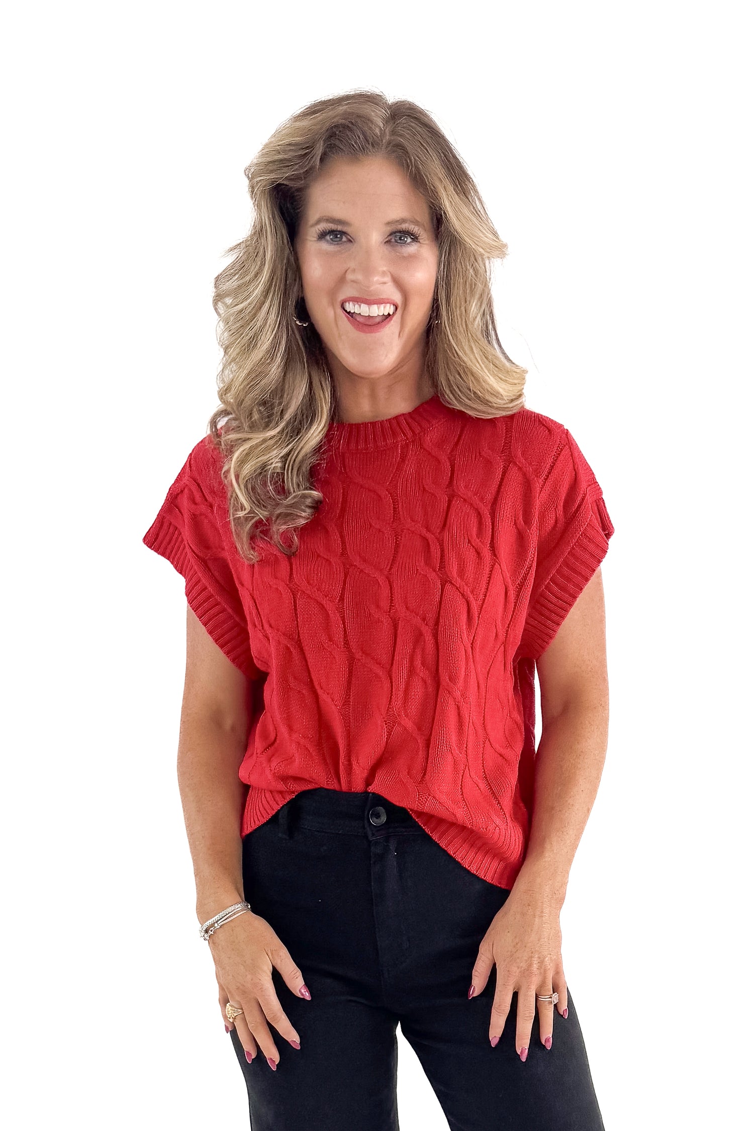 Front view of woman wearing red sleeveless sweater with jeans against white studio background.