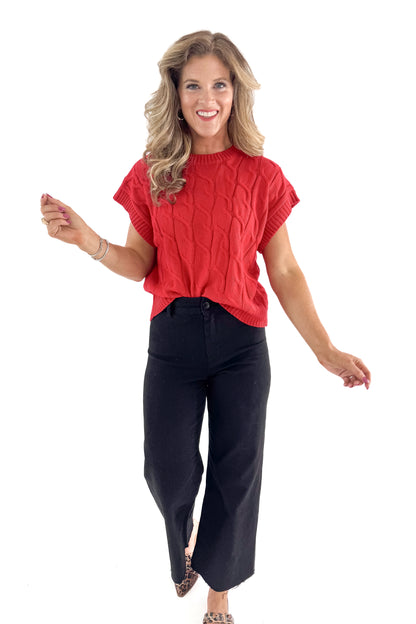 Front view of woman wearing red sleeveless sweater with jeans against white studio background.
